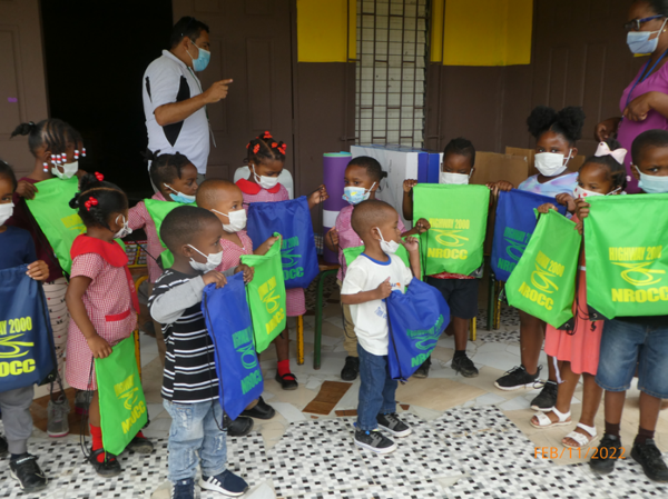 Some students at Alexander Basic School displaying one of the gifts donated by NROCC. In the background: Mr. Raul Brito, Resident Engineer for the May Pen to Williamsfield leg of Highway 2000 and Mrs. Claudia Baker, Principal – Alexander Basic School.